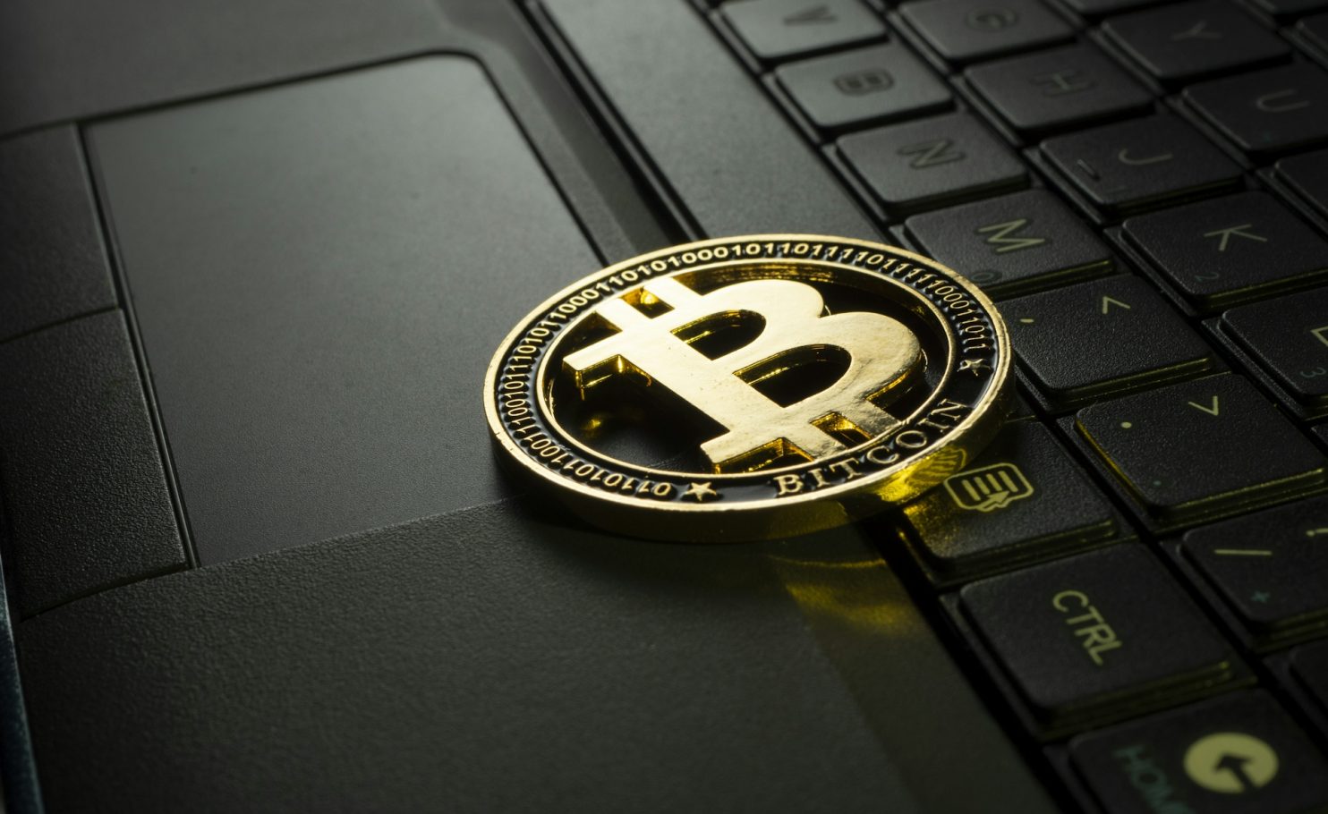 Goldene Bitcoin-Münze liegt auf einer Laptop-Tastatur.